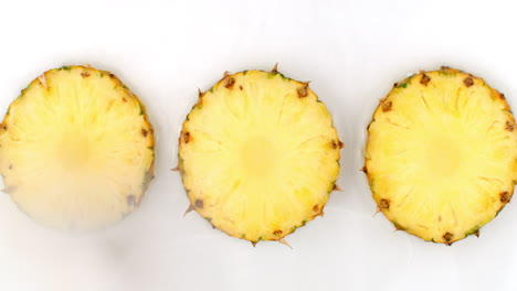 Top-view:-3-slices-of-pineapple-washed-with-water-on-a-white-background.-Water-splashes-in-slow-motion.